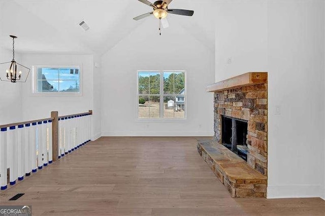 unfurnished living room featuring lofted ceiling, a stone fireplace, wood-type flooring, and ceiling fan with notable chandelier