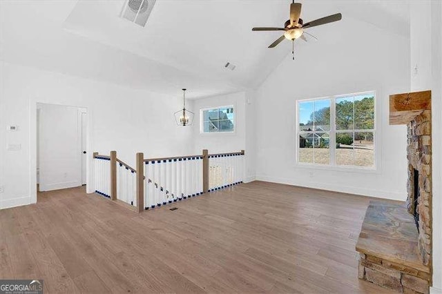 unfurnished living room with wood-type flooring, a stone fireplace, ceiling fan with notable chandelier, and high vaulted ceiling