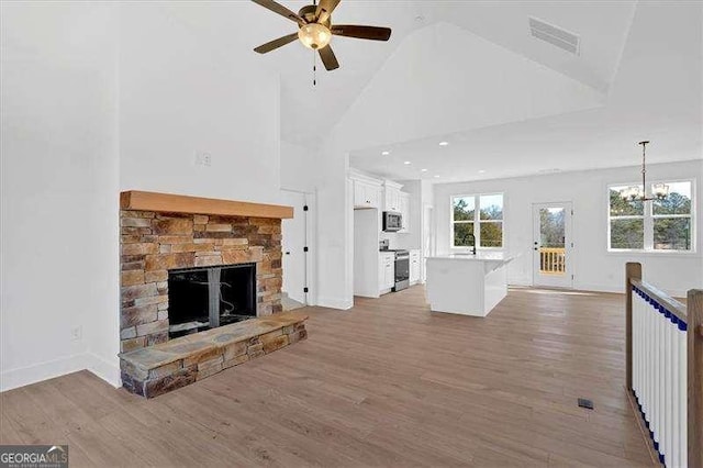 unfurnished living room featuring high vaulted ceiling, a healthy amount of sunlight, a fireplace, and light hardwood / wood-style flooring