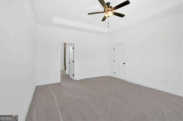 empty room with ceiling fan and a raised ceiling