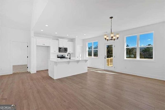 kitchen with pendant lighting, appliances with stainless steel finishes, a kitchen breakfast bar, an island with sink, and white cabinets