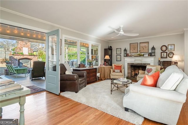 living room with crown molding, a fireplace, light wood-style flooring, and ceiling fan