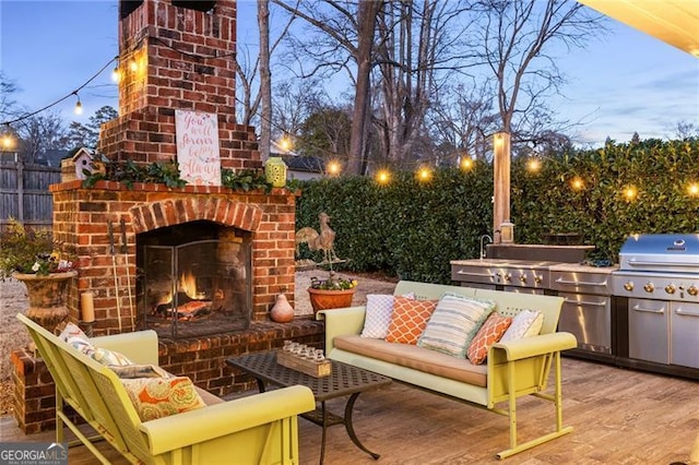 patio terrace at dusk with an outdoor brick fireplace, an outdoor kitchen, and a grill