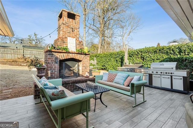 view of patio with grilling area, an outdoor living space with a fireplace, fence, a deck, and exterior kitchen