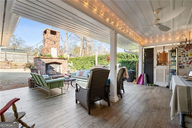 view of patio / terrace with an outdoor living space with a fireplace, ceiling fan, fence, and a deck