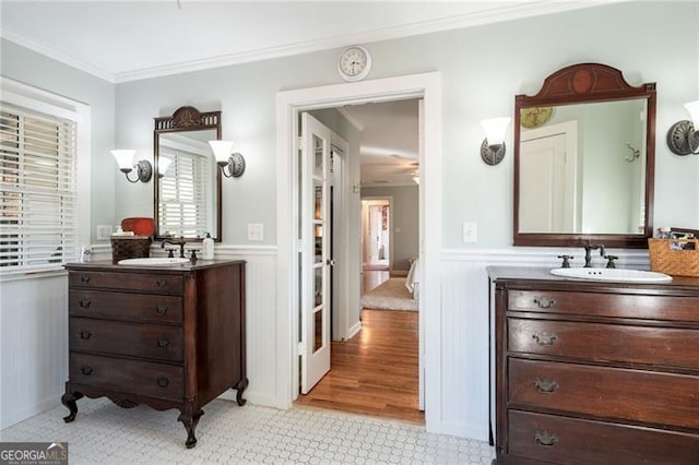 bathroom featuring two vanities, a wainscoted wall, a sink, and crown molding