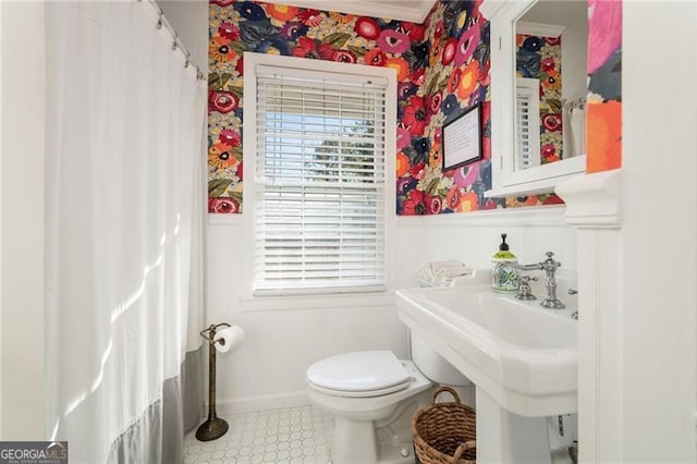 bathroom featuring toilet, a wainscoted wall, a sink, and wallpapered walls