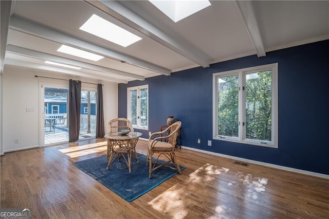 dining room with beamed ceiling, a skylight, and hardwood / wood-style floors