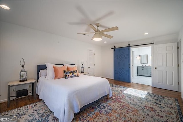 bedroom featuring ensuite bathroom, a barn door, dark hardwood / wood-style floors, and ceiling fan