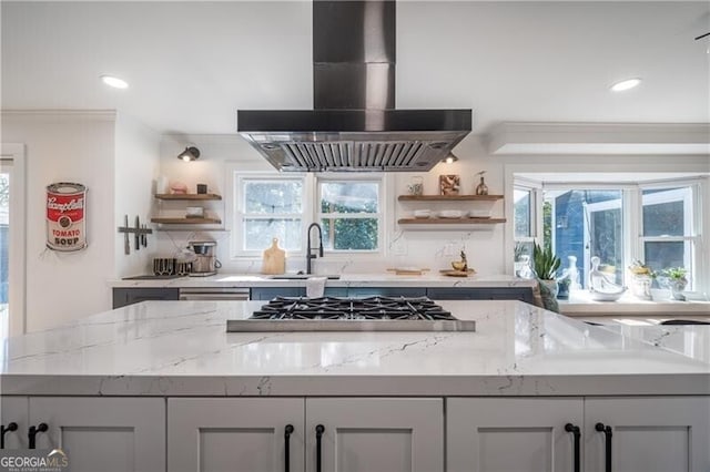 kitchen with sink, island exhaust hood, stainless steel gas cooktop, light stone counters, and a healthy amount of sunlight