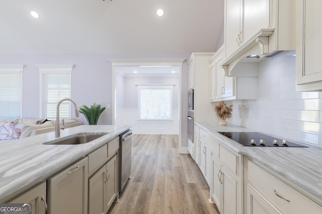 kitchen featuring sink, decorative backsplash, light stone counters, stainless steel appliances, and light hardwood / wood-style flooring