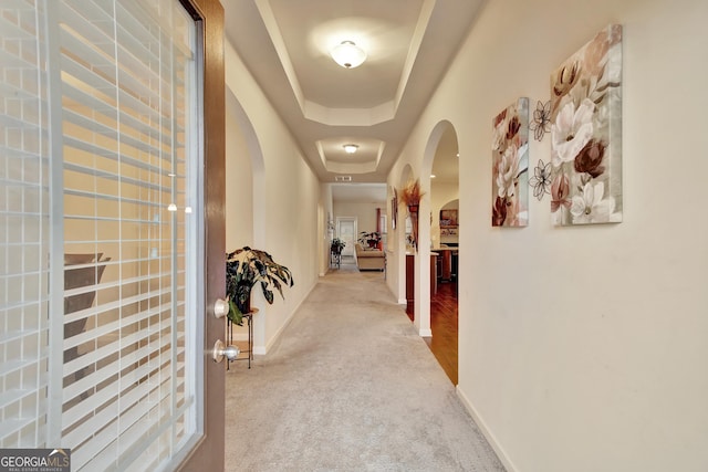 hall with a raised ceiling and light carpet