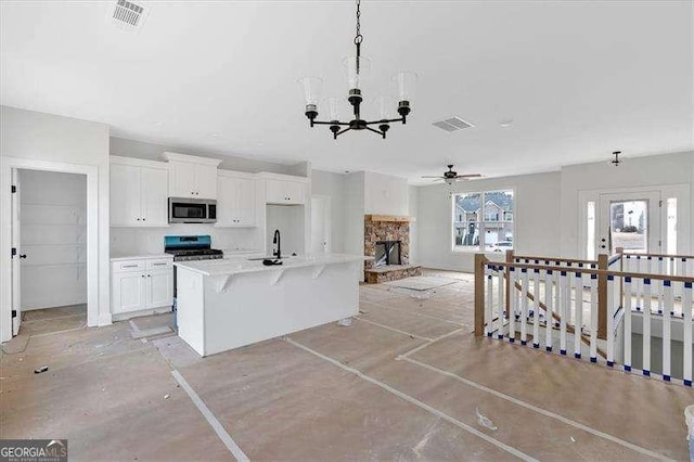 kitchen with a stone fireplace, pendant lighting, white cabinetry, a kitchen island with sink, and stainless steel appliances