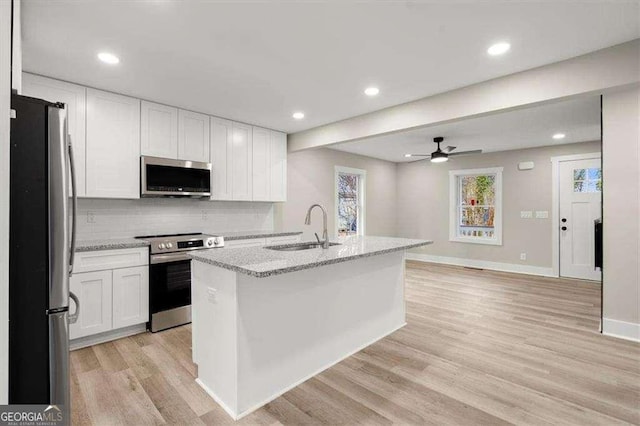 kitchen featuring stainless steel appliances, white cabinetry, a kitchen island with sink, and light stone counters