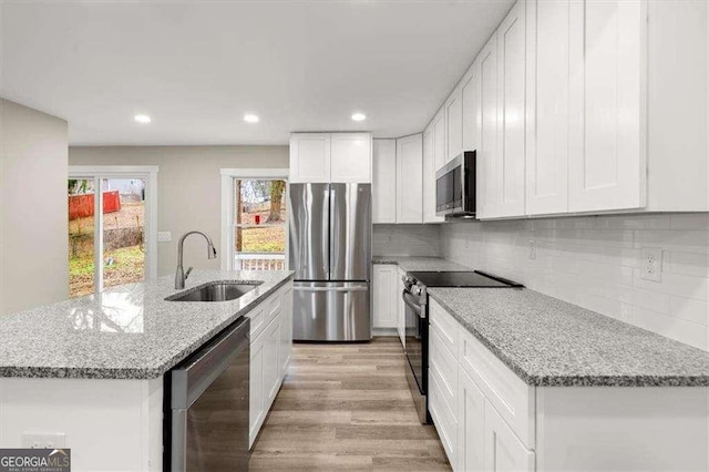 kitchen featuring appliances with stainless steel finishes, white cabinetry, an island with sink, sink, and light stone counters