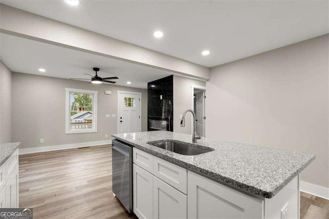 kitchen featuring sink, white cabinetry, light stone counters, stainless steel dishwasher, and an island with sink