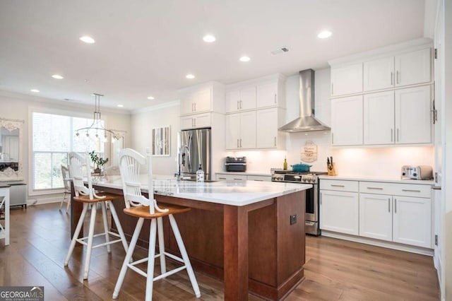 kitchen with an island with sink, appliances with stainless steel finishes, white cabinets, and wall chimney exhaust hood