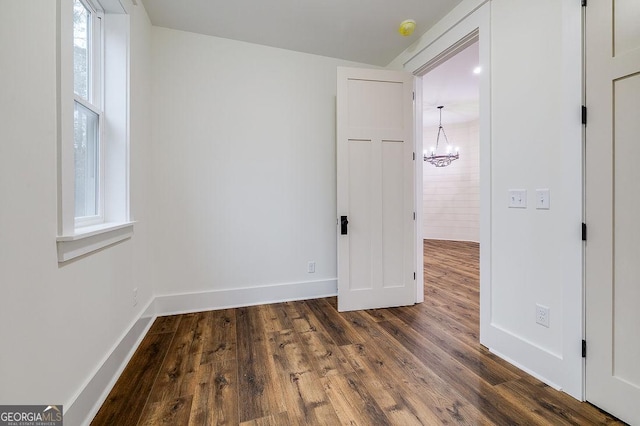 empty room with dark hardwood / wood-style flooring and an inviting chandelier