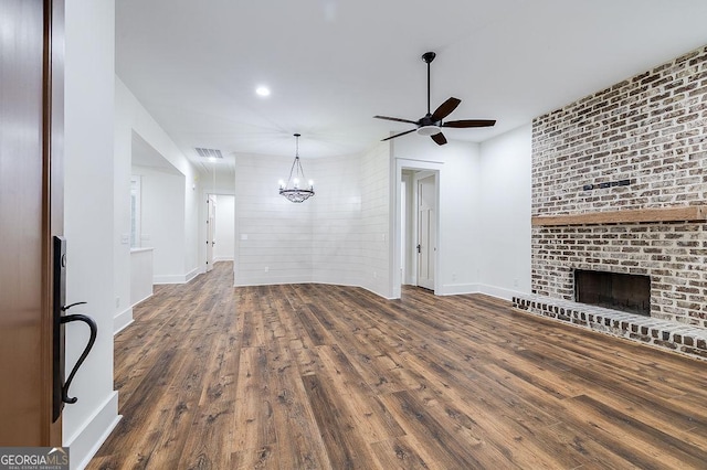 unfurnished living room with dark hardwood / wood-style flooring, ceiling fan with notable chandelier, and a fireplace