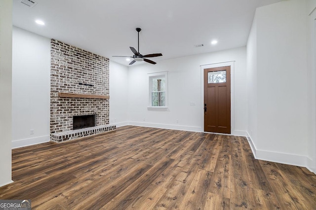 unfurnished living room with a brick fireplace, dark wood-type flooring, and ceiling fan