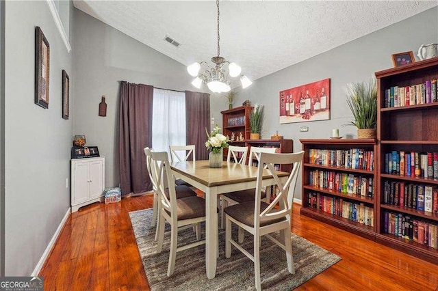 dining space with wood-type flooring, vaulted ceiling, a textured ceiling, and a notable chandelier