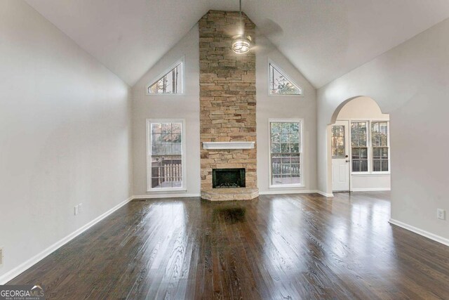 unfurnished living room featuring dark wood-type flooring, a stone fireplace, and high vaulted ceiling