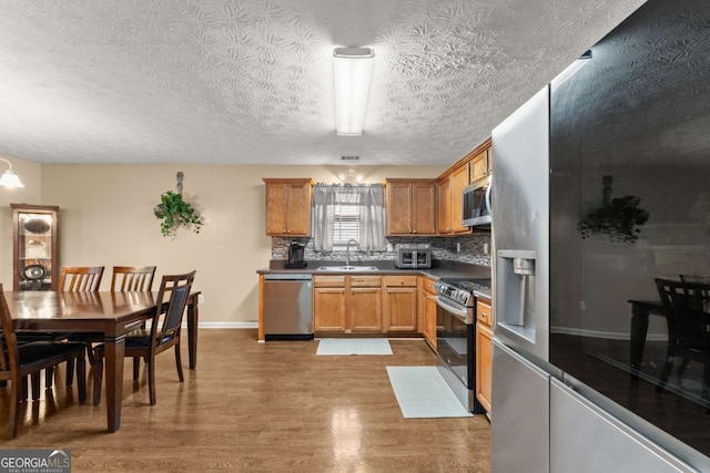 kitchen featuring appliances with stainless steel finishes, tasteful backsplash, sink, light hardwood / wood-style floors, and a textured ceiling