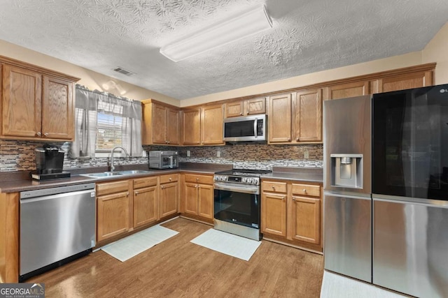 kitchen featuring sink, stainless steel appliances, tasteful backsplash, a textured ceiling, and light wood-type flooring