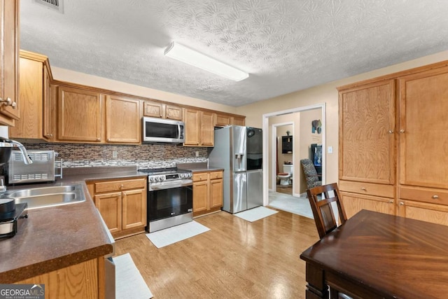 kitchen featuring sink, light hardwood / wood-style flooring, stainless steel appliances, tasteful backsplash, and a textured ceiling