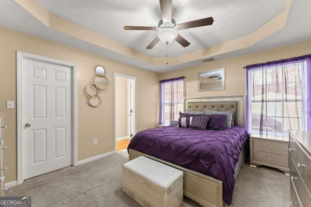 bedroom with multiple windows, light colored carpet, ceiling fan, and a tray ceiling