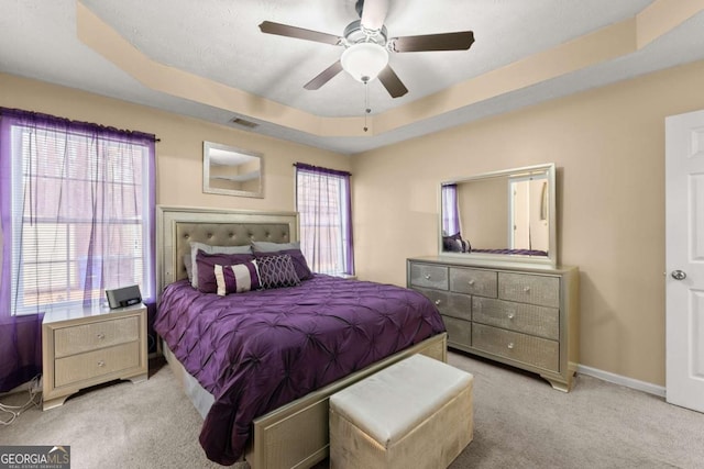 carpeted bedroom with multiple windows, a raised ceiling, and ceiling fan