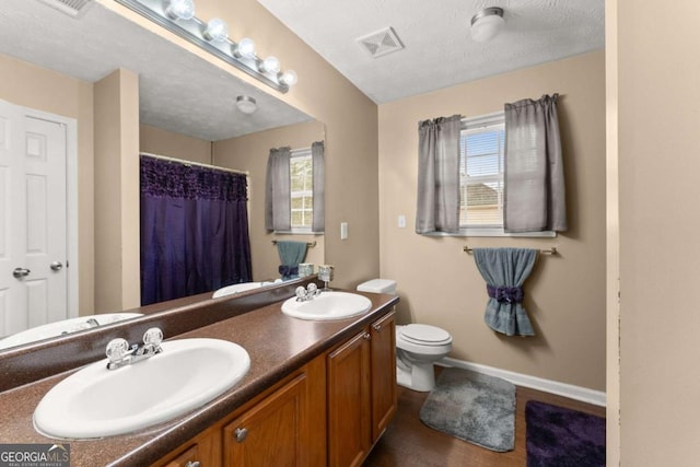 bathroom featuring vanity, a textured ceiling, toilet, and a healthy amount of sunlight