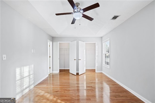 unfurnished bedroom with multiple closets, ceiling fan, a tray ceiling, and light hardwood / wood-style floors