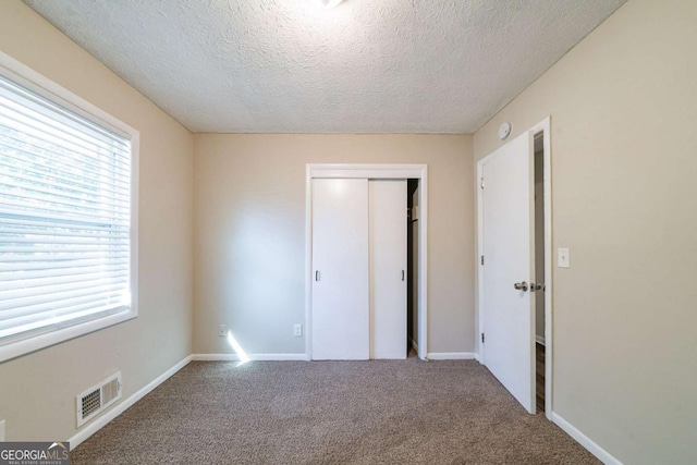 unfurnished bedroom featuring multiple windows, carpet, a textured ceiling, and a closet