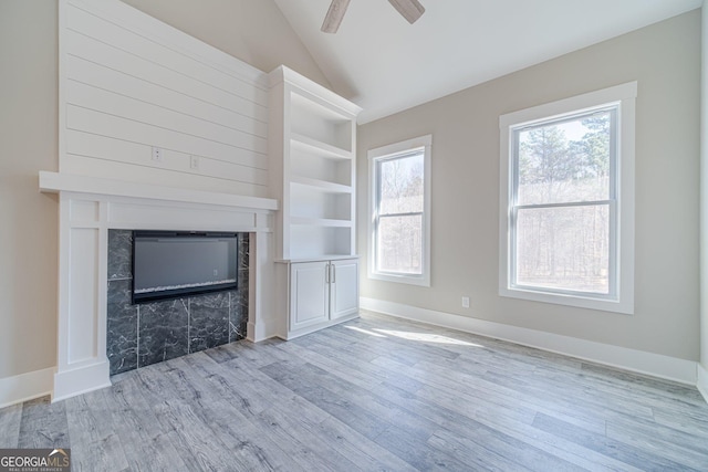 unfurnished living room with a ceiling fan, a glass covered fireplace, vaulted ceiling, wood finished floors, and baseboards