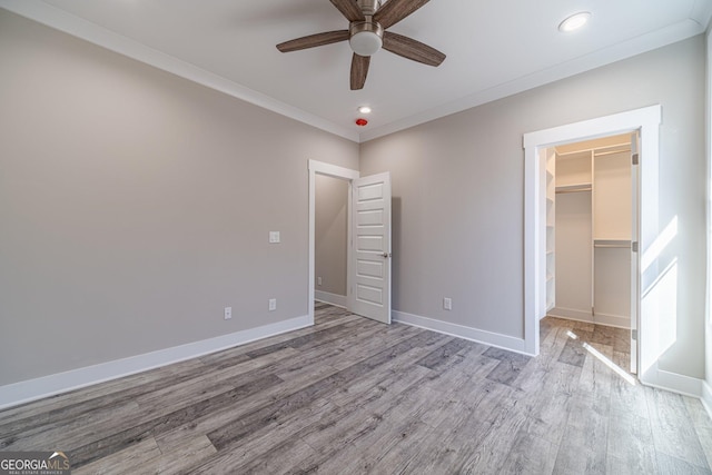 unfurnished bedroom featuring baseboards, wood finished floors, a walk in closet, crown molding, and recessed lighting