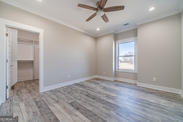 unfurnished bedroom with wood finished floors, ornamental molding, baseboards, a walk in closet, and recessed lighting