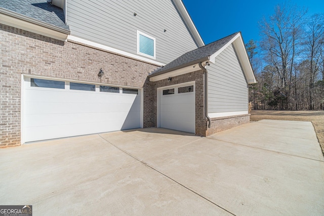 view of property exterior featuring driveway, roof with shingles, and brick siding