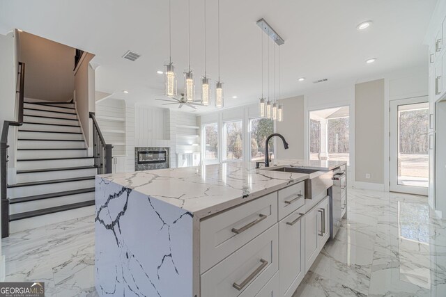 kitchen featuring a spacious island, white cabinetry, light stone counters, hanging light fixtures, and a large fireplace