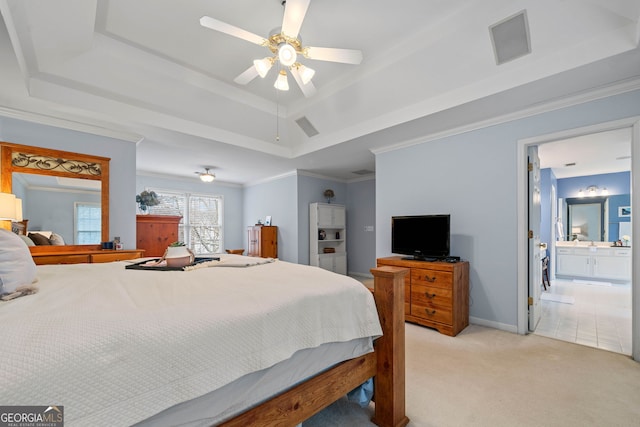 bedroom featuring light carpet, a tray ceiling, ensuite bath, and ceiling fan