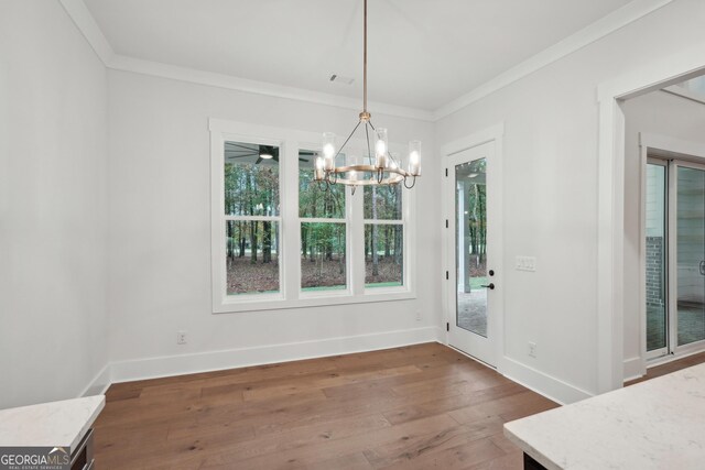 unfurnished dining area featuring crown molding, dark hardwood / wood-style floors, and an inviting chandelier