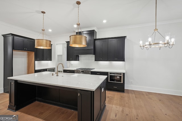 kitchen featuring sink, tasteful backsplash, decorative light fixtures, a kitchen island with sink, and light hardwood / wood-style floors