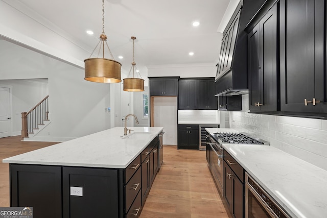 kitchen featuring a kitchen island with sink, hanging light fixtures, light stone counters, and ornamental molding