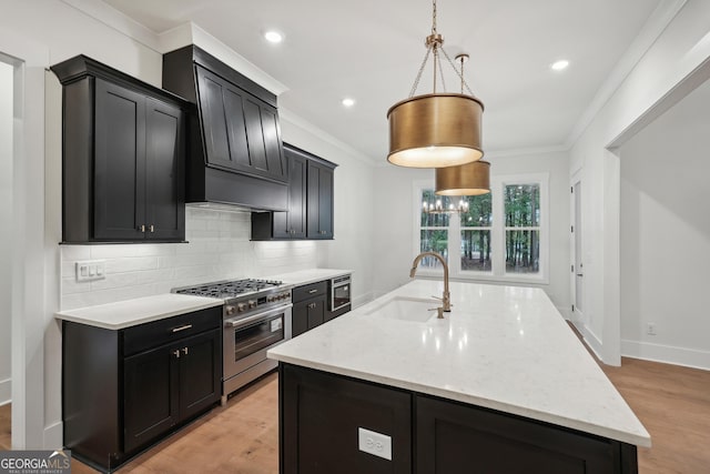 kitchen featuring sink, light stone counters, decorative light fixtures, a center island with sink, and stainless steel stove