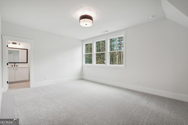 unfurnished bedroom featuring vaulted ceiling, light colored carpet, and ensuite bath