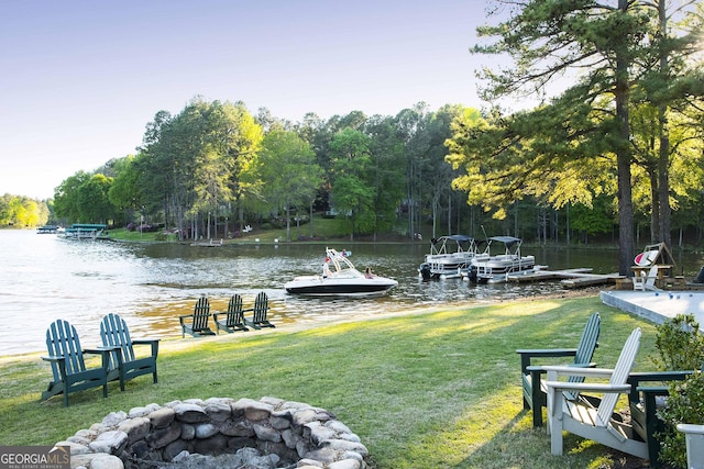 dock area featuring a water view, a fire pit, and a lawn