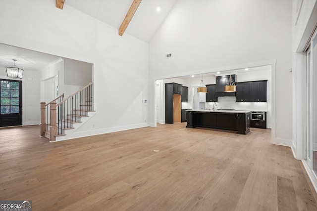 living room featuring sink, beam ceiling, high vaulted ceiling, a chandelier, and light wood-type flooring