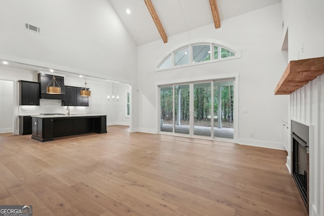 unfurnished living room with beam ceiling, an inviting chandelier, high vaulted ceiling, and light hardwood / wood-style flooring