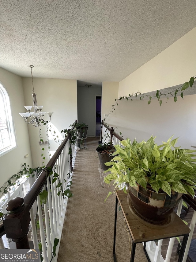 hallway featuring an inviting chandelier, a textured ceiling, and carpet