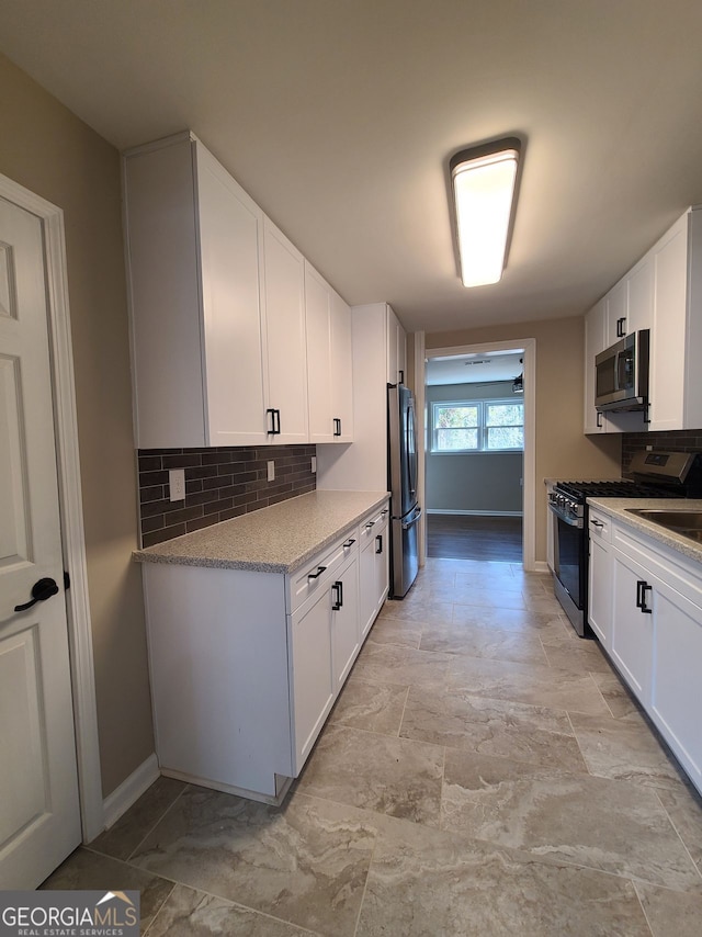 kitchen featuring stainless steel appliances, white cabinetry, backsplash, and light stone counters